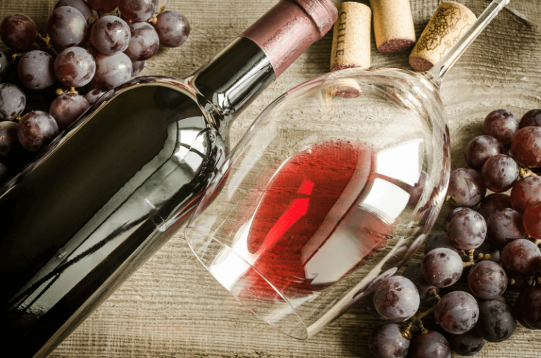 butelka czerwonego wina z kieliszkiem czerwonego wina leżące na stole