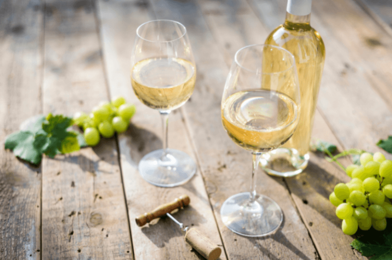 dwa kieliszki białego wina na stole obok kiści białych winogron